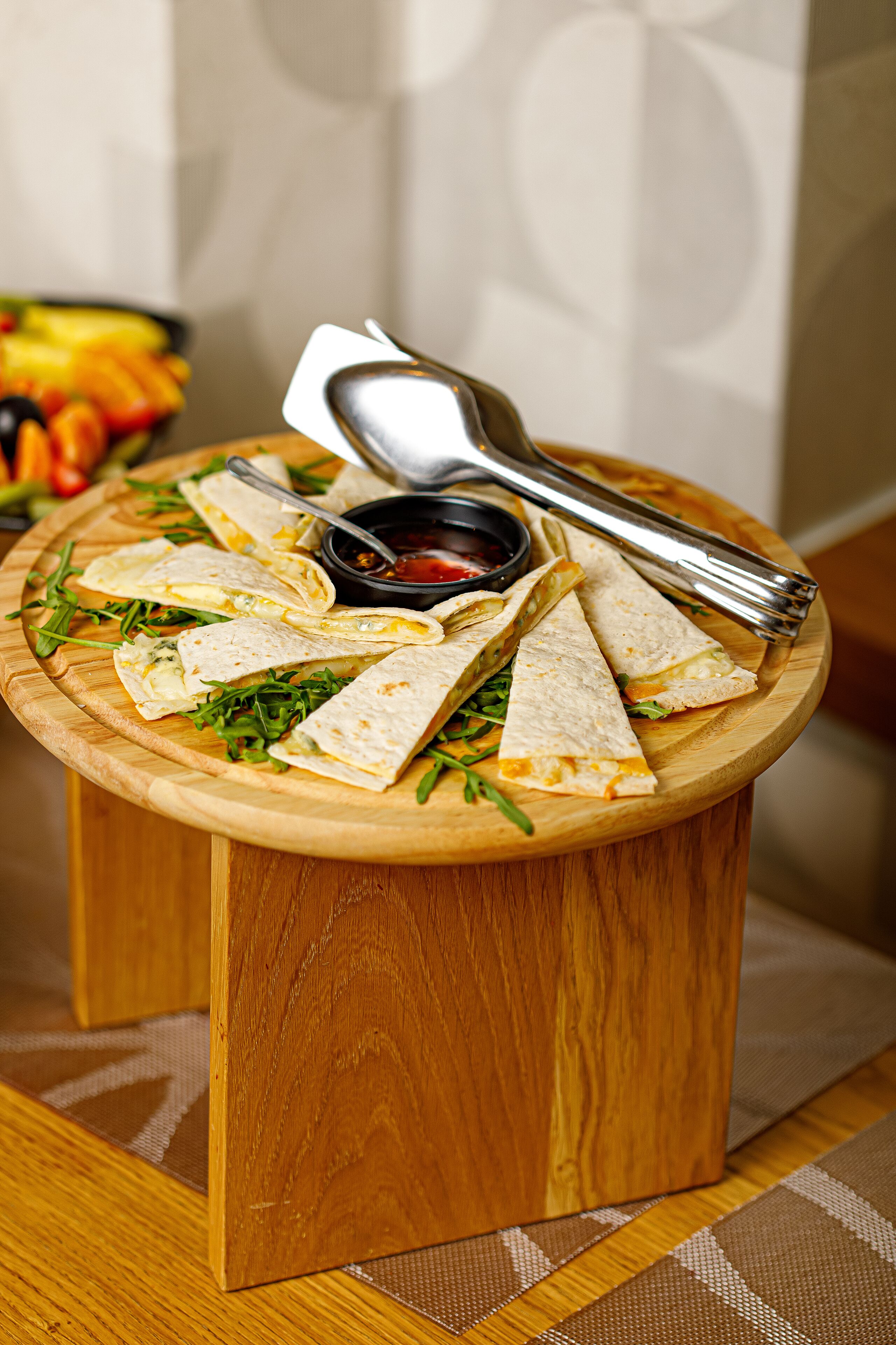 A wooden table with a plate of quesadillas and a bowl of salsa.