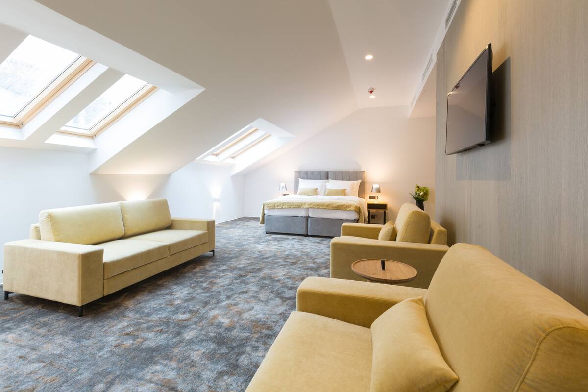 A modern bedroom with a large bed, a sofa, and a TV mounted on the wall.