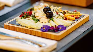 A wooden board with a variety of cheeses, olives, and flowers, accompanied by a glass of white wine and bottles of olive oil.