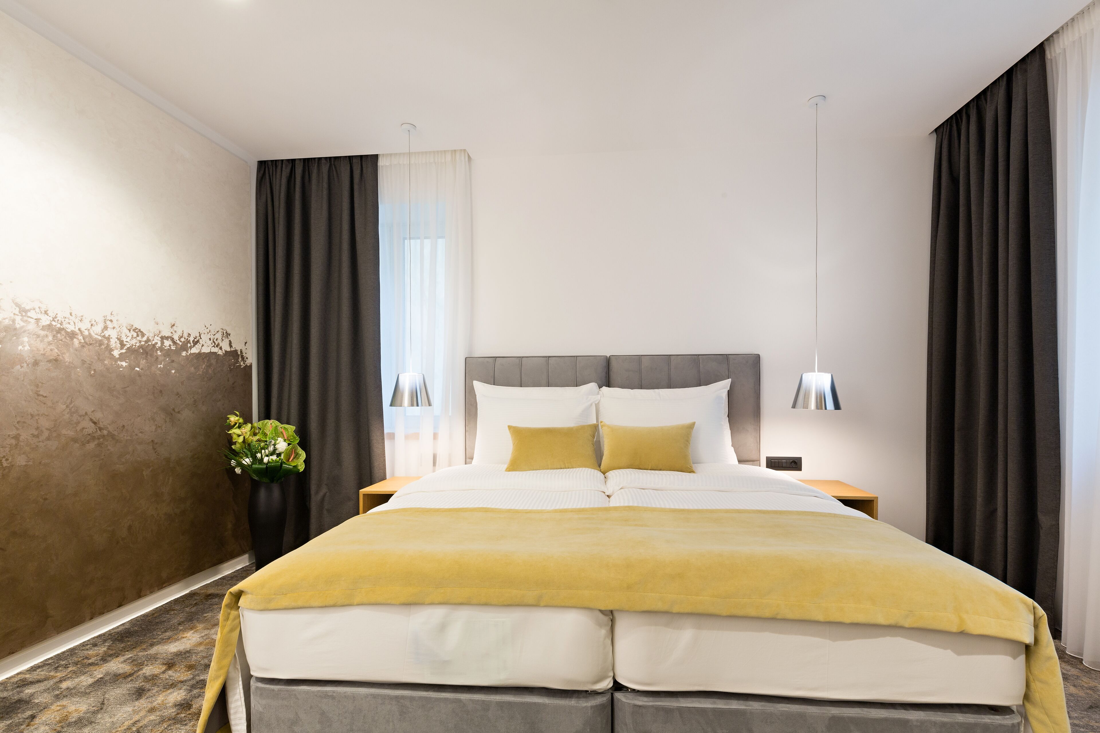 A modern hotel room with a large bed, a bedside table, a lamp, and a vase with flowers.