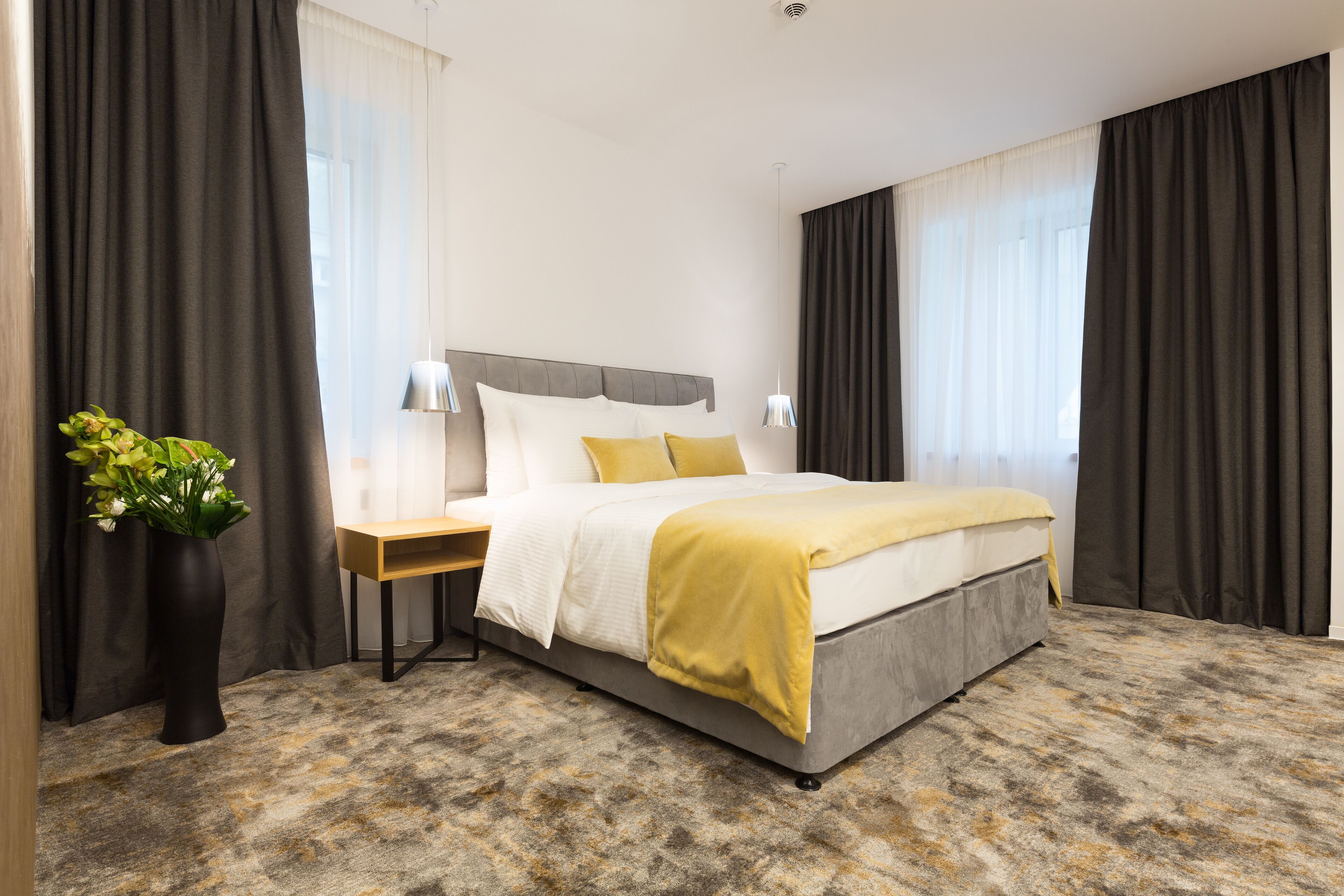 A modern hotel room with a large bed, a bedside table, a lamp, and a potted plant.