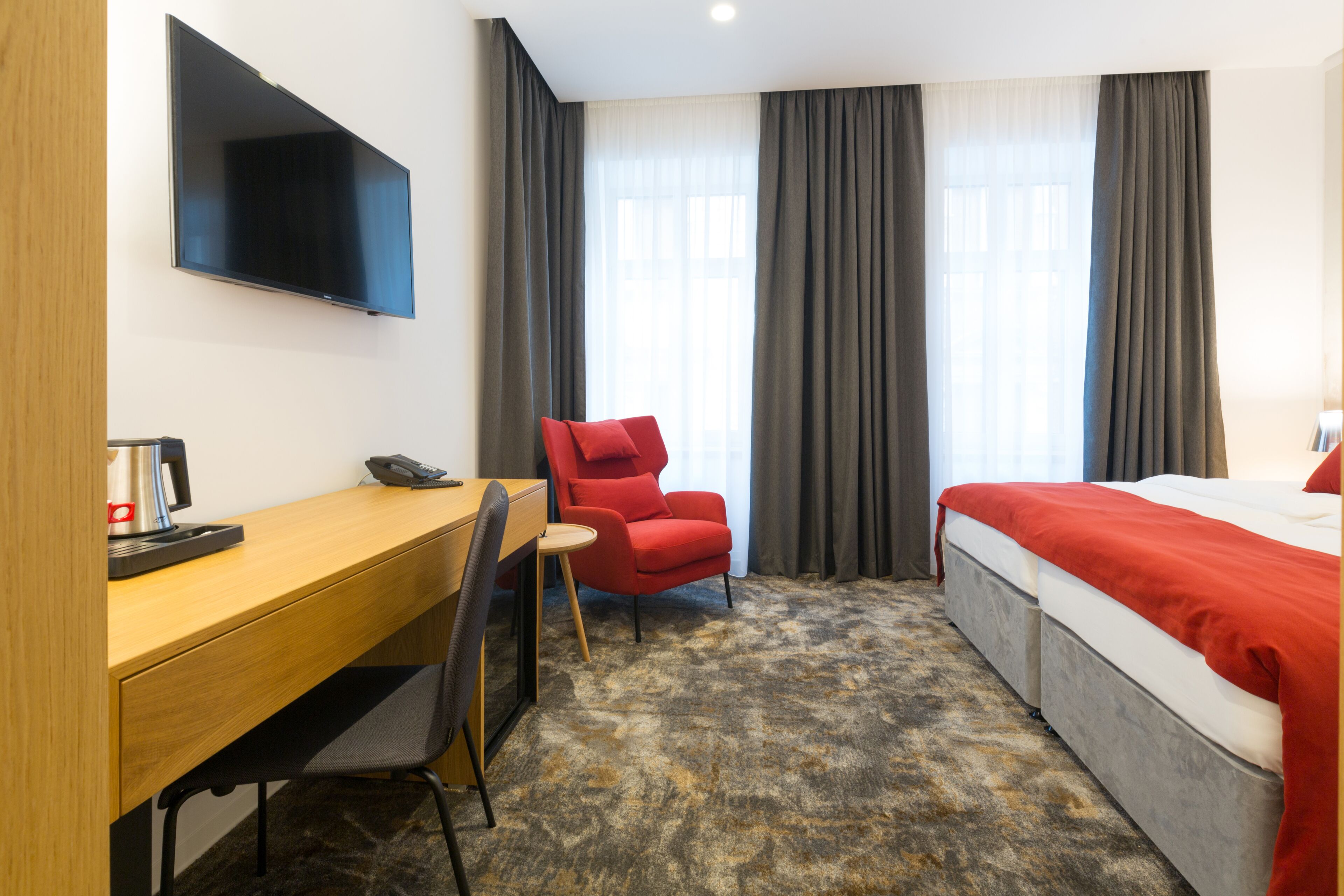 Una habitación de hotel con cama, escritorio, silla, televisor y ventana con cortinas.