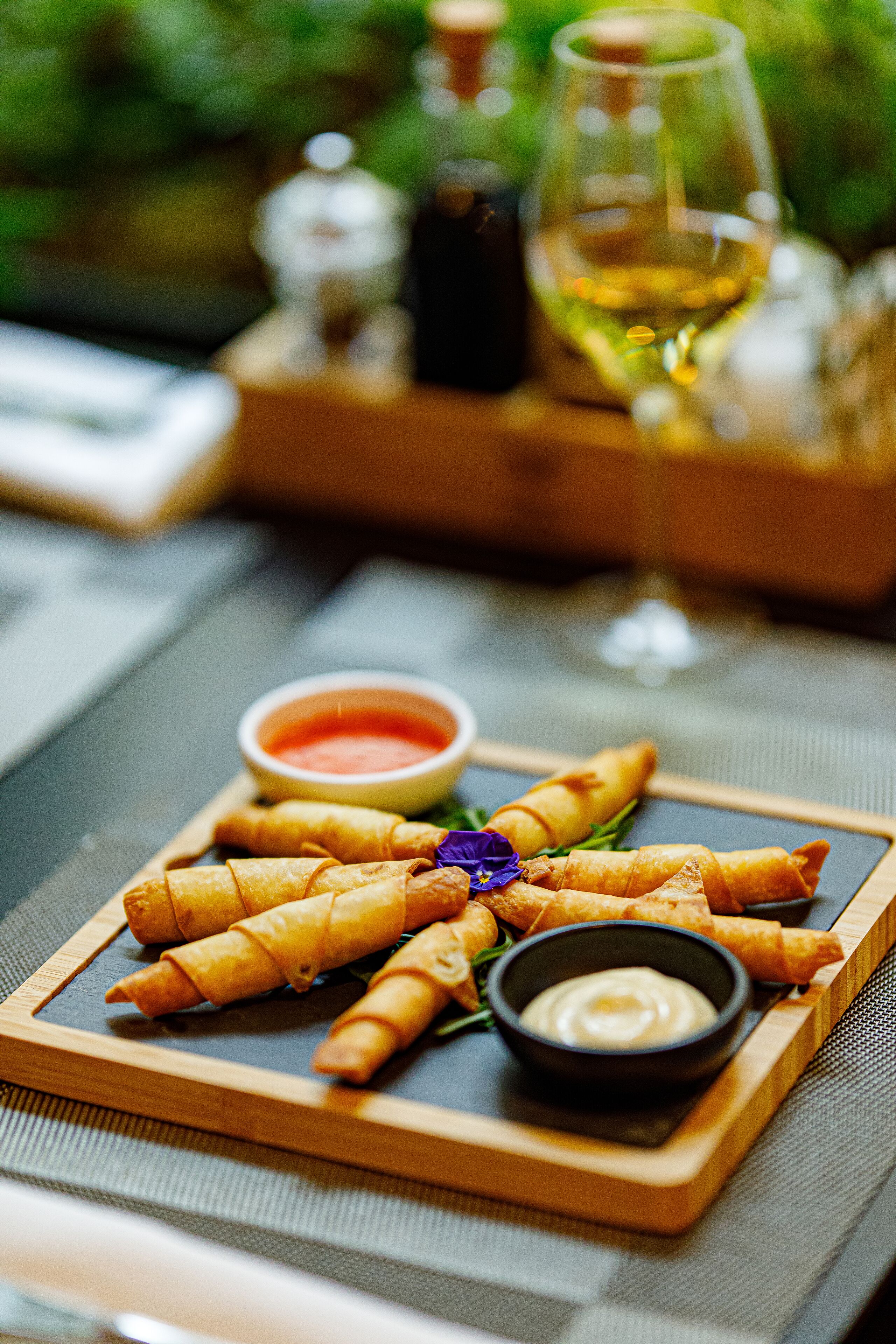 A tray of spring rolls with dipping sauces on a wooden board.