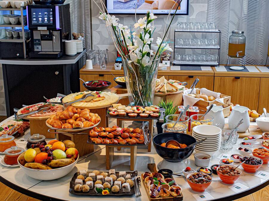 A buffet table with various food items, a coffee station, and a television displaying a room interior.
