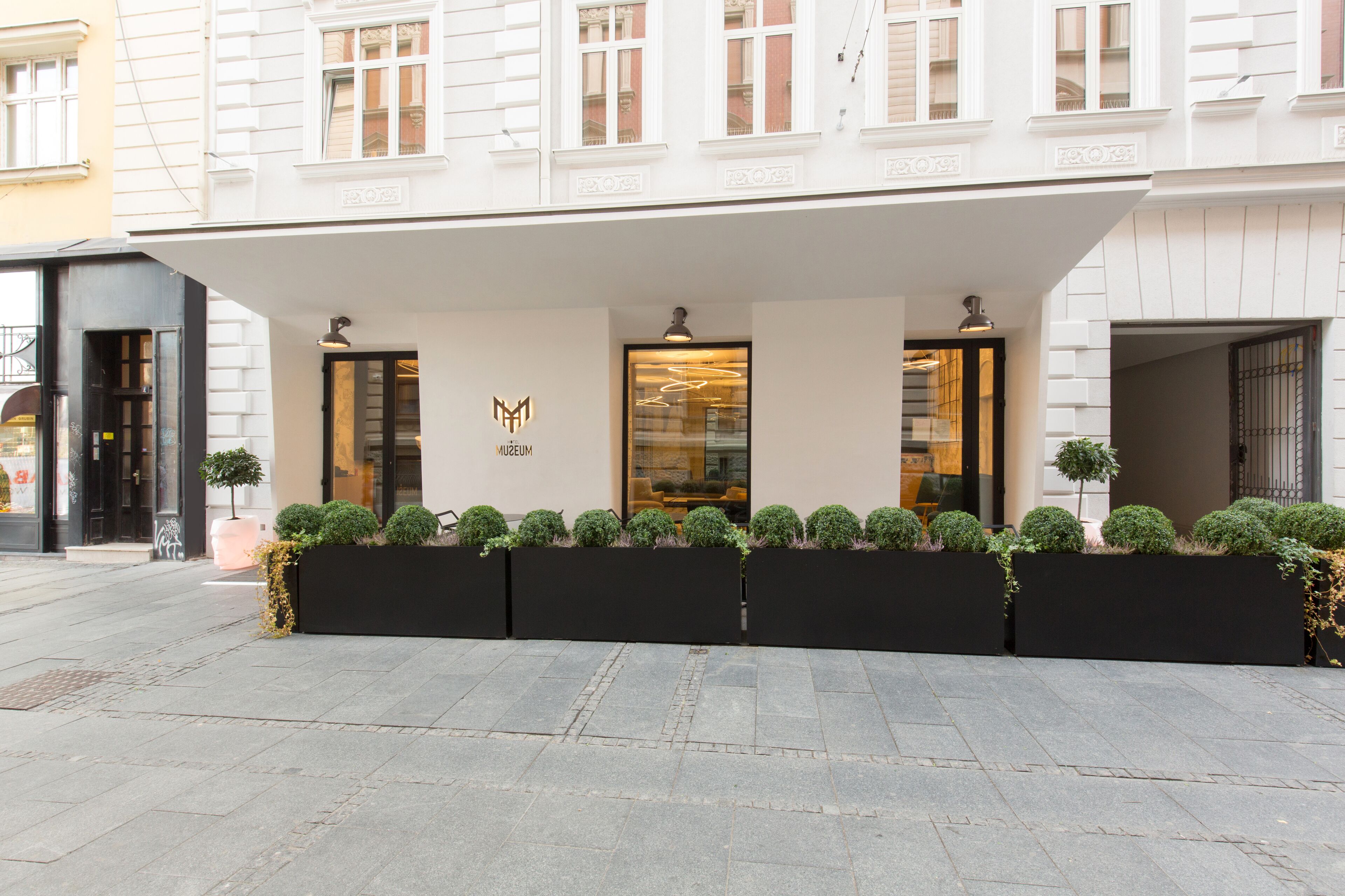 A modern building with a white facade, a black awning, and a logo on the front.