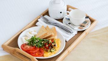 Bandeja de desayuno con tostadas, huevos, tomates y verduras sobre una cama.