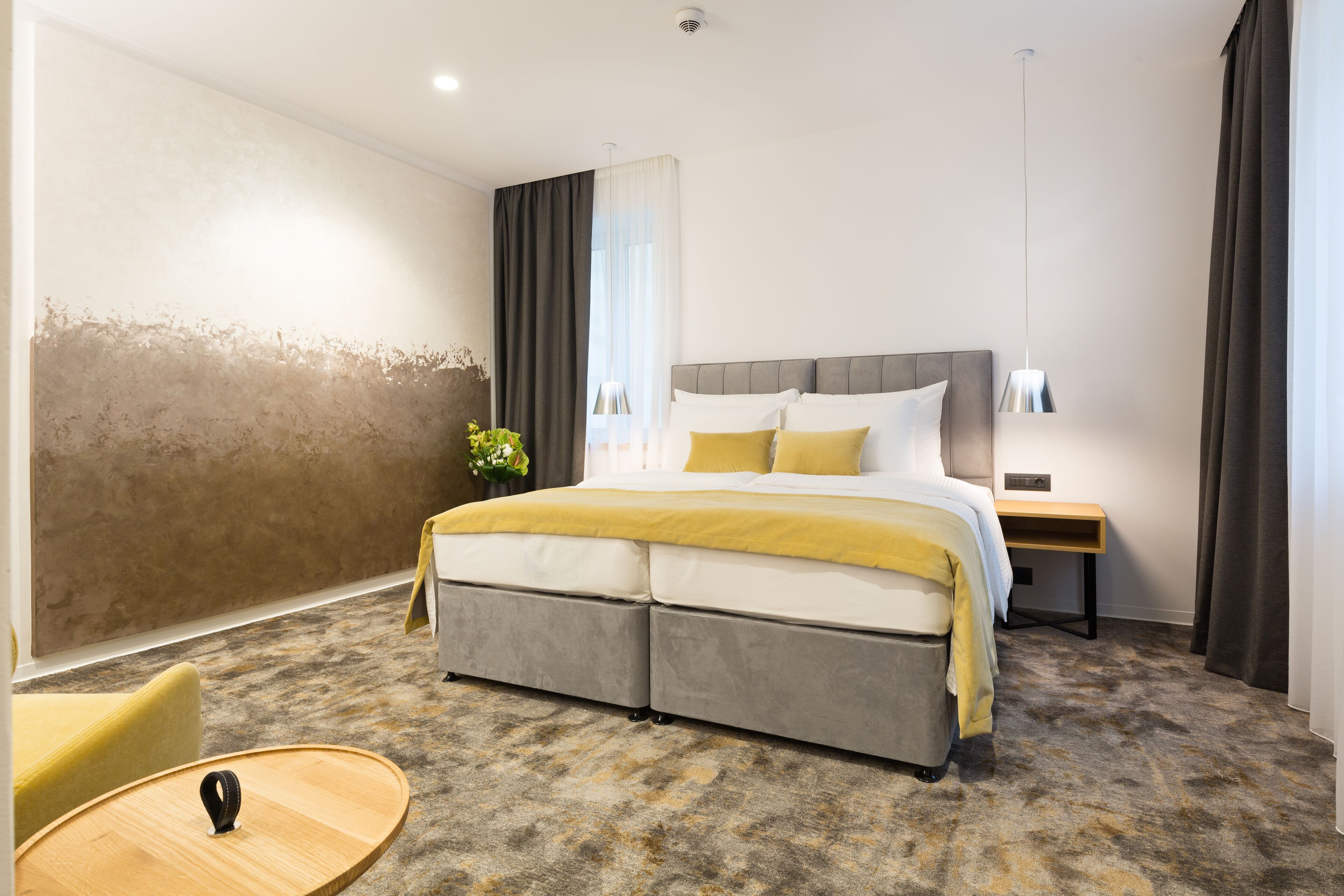 A modern hotel room with a large bed, a bedside table, a chair, and a small round table.