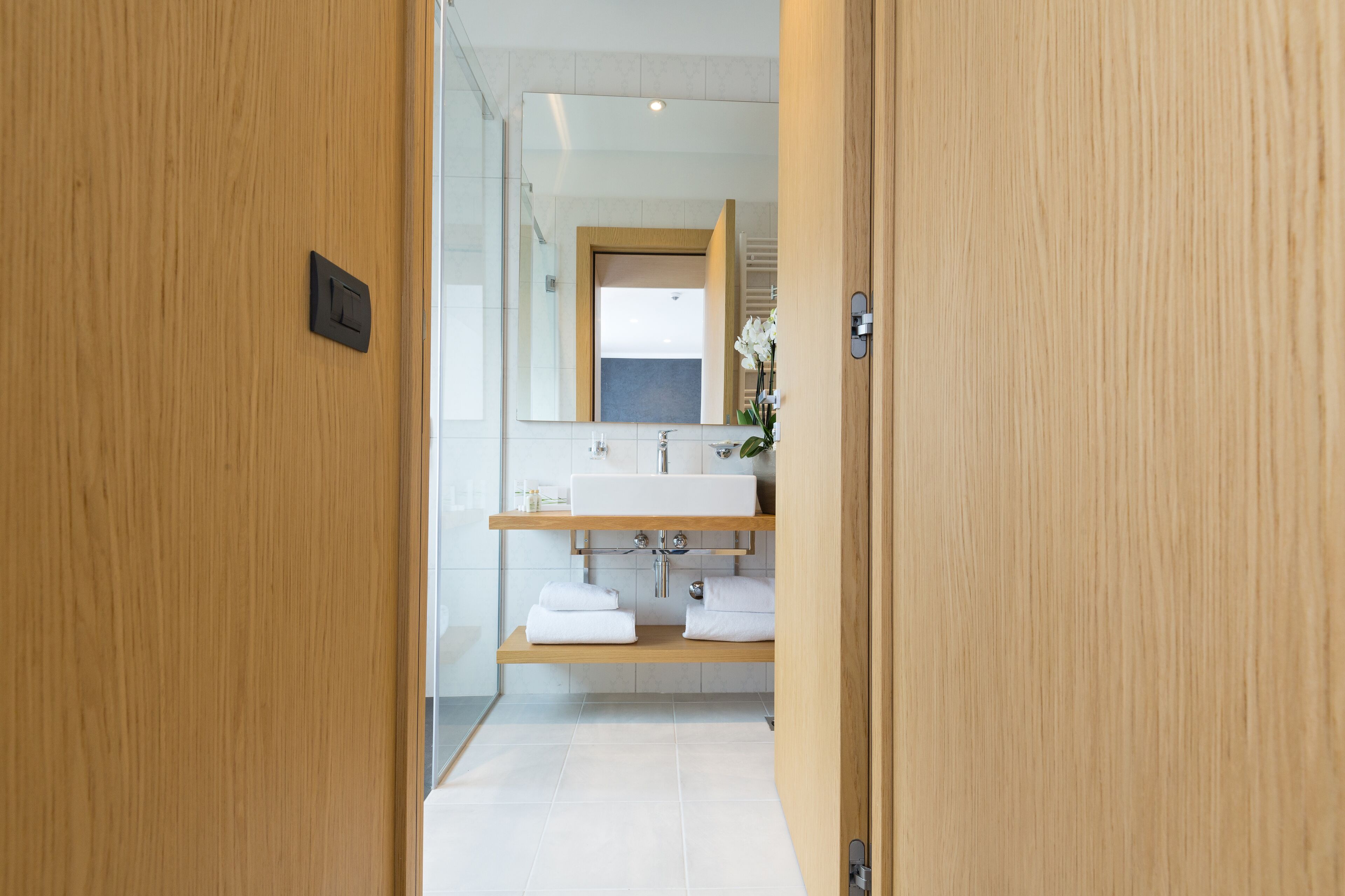 Une salle de bain moderne avec une porte en bois, un lavabo blanc et un miroir au-dessus.