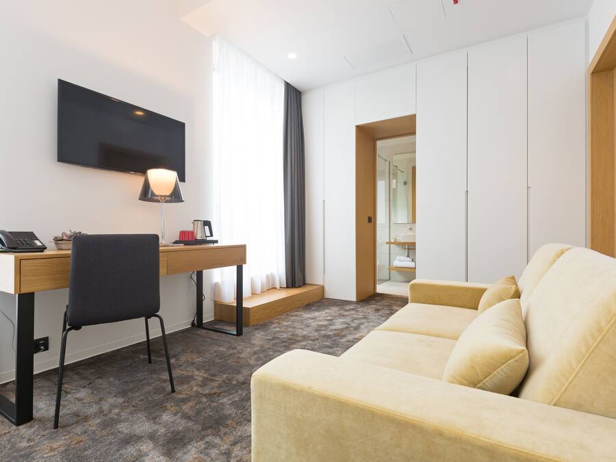 A modern hotel room with a desk, chair, and sofa.