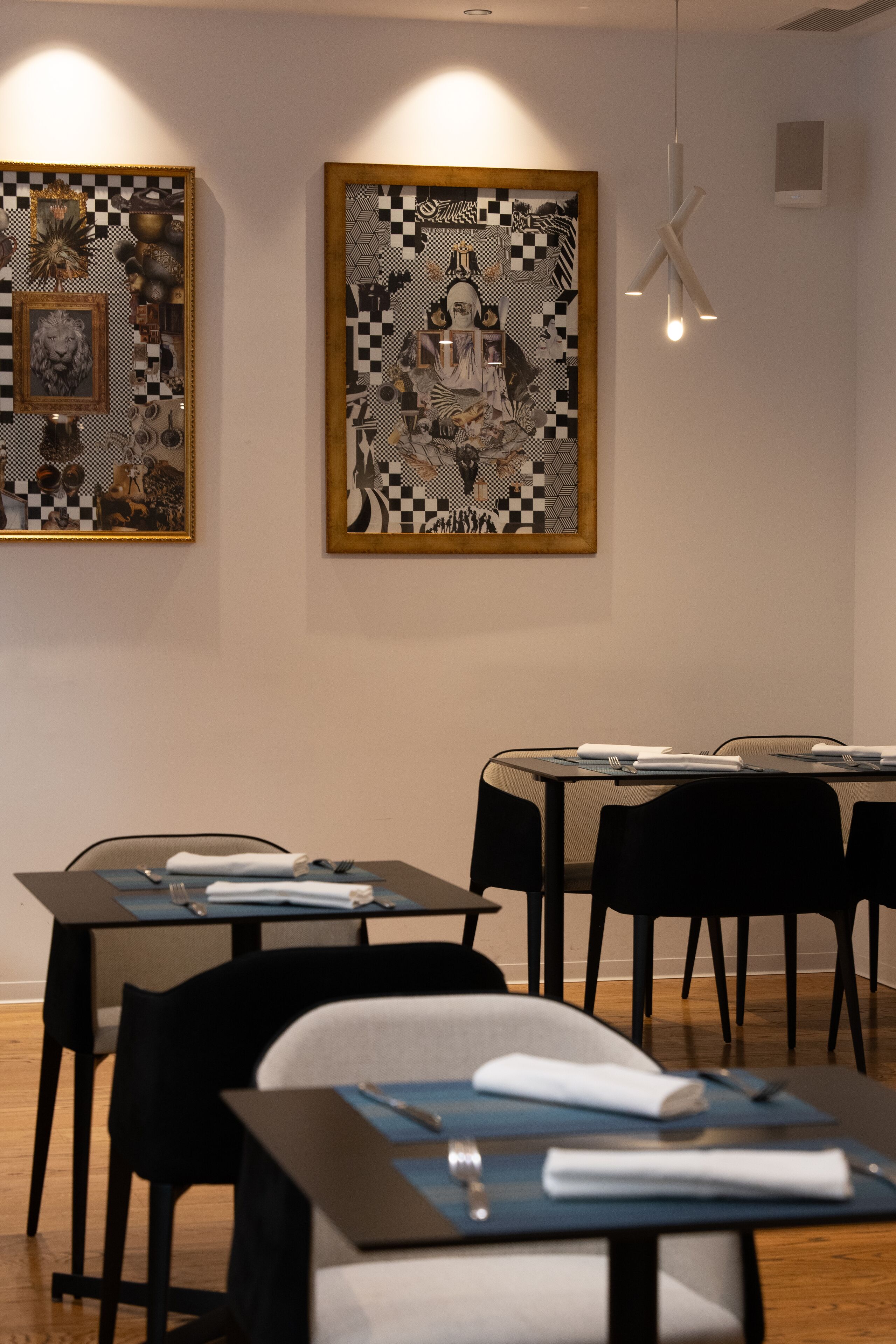 A dining area with tables and chairs, framed artwork on the walls, and a hanging light fixture.
