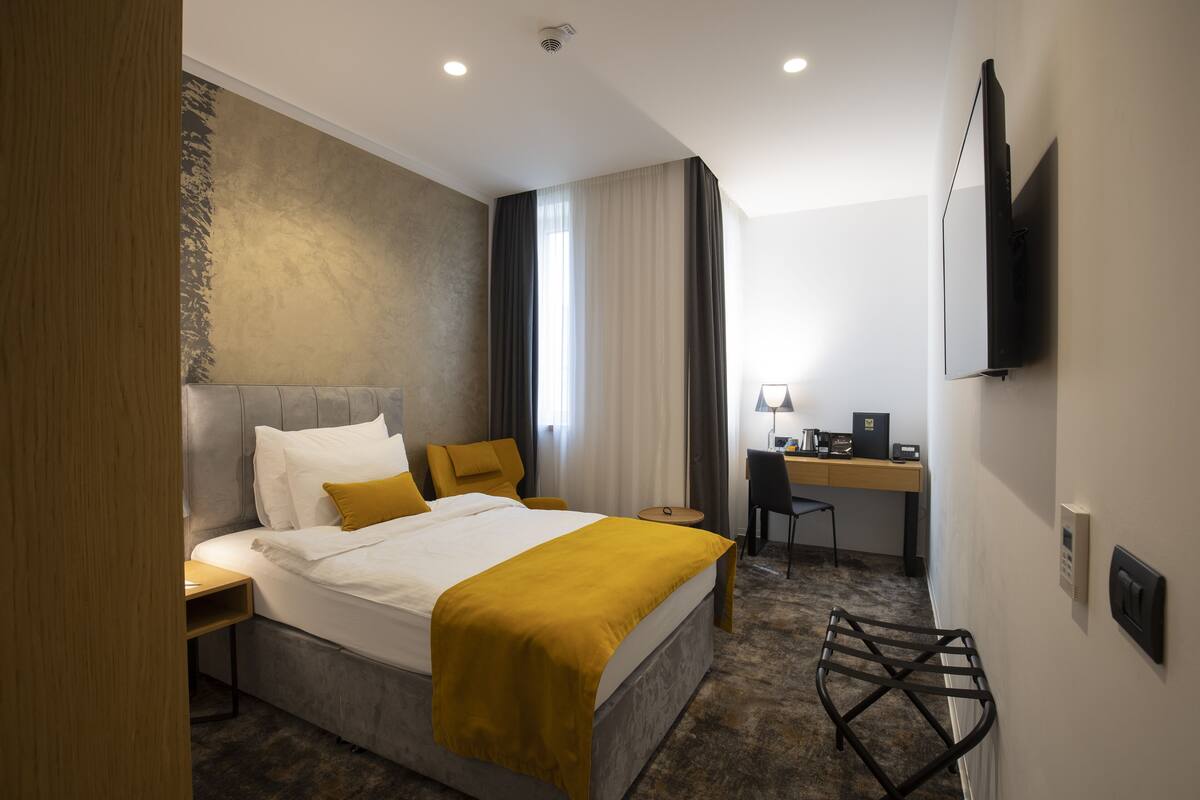 A hotel room with a bed, a desk, a chair, a television, and a control panel.