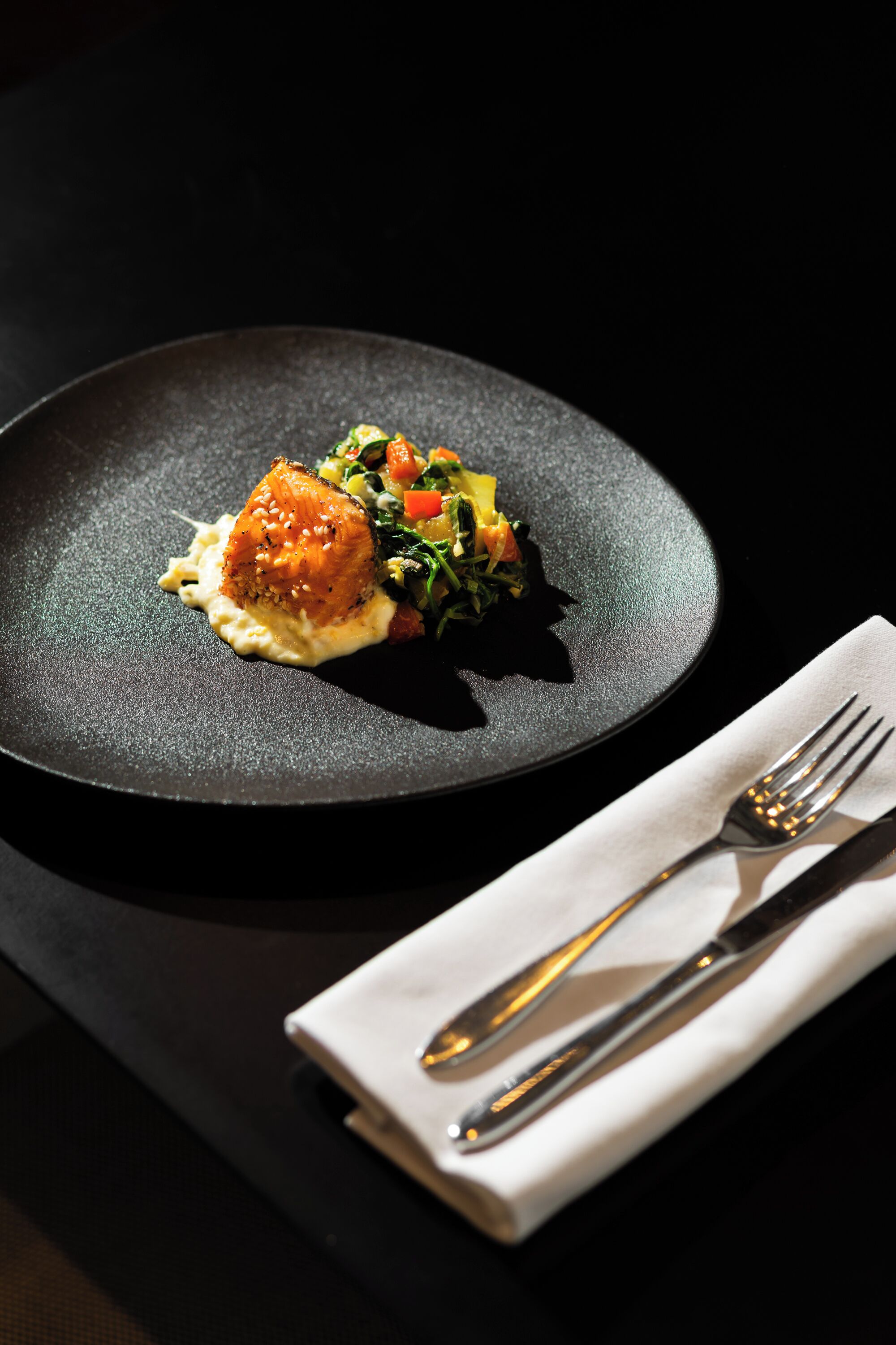 A plate of food on a dark table with a fork and napkin on a white napkin holder.