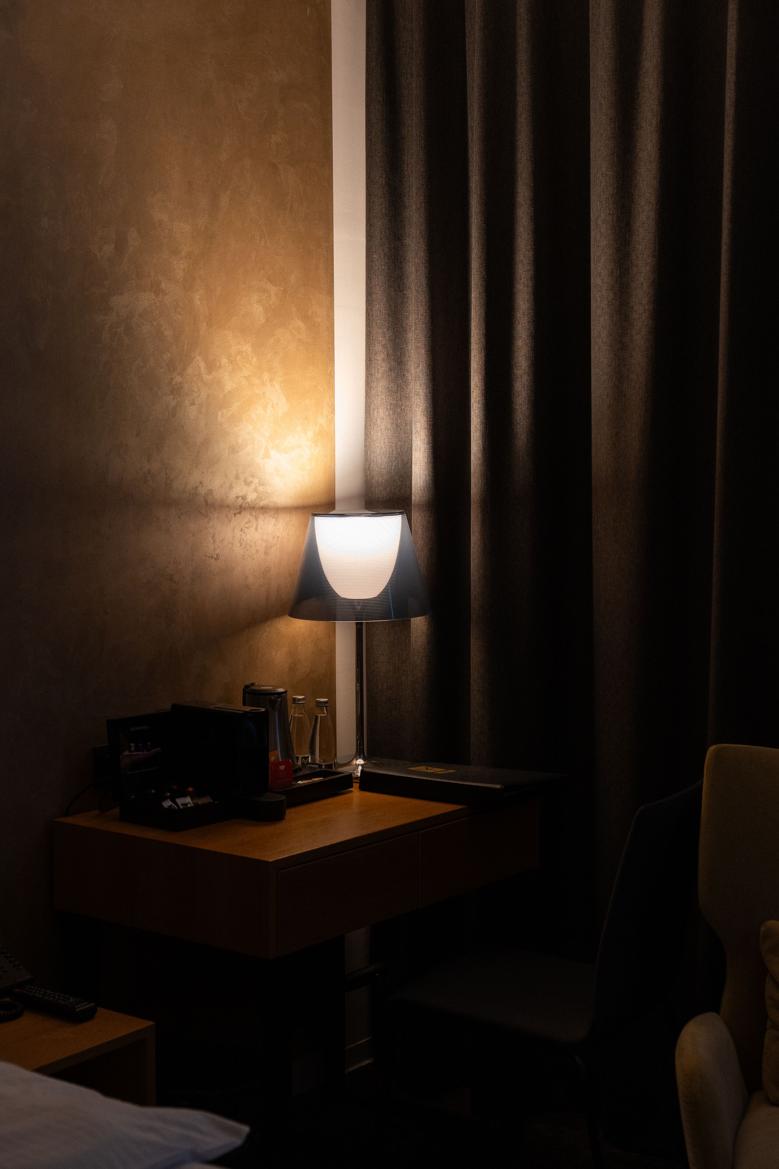 Una camera d'albergo con una scrivania, una lampada, un telecomando e una sedia.