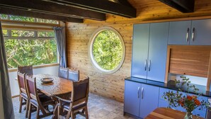 Un coin repas avec une table et des chaises en bois, une fenêtre ronde et une cuisine aux armoires bleues.