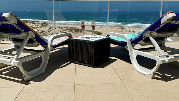 Ein Balkon mit zwei Liegestühlen, einem kleinen Tisch und einem Glas Wein. Blick auf Strand und Meer.