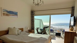 Ein Schlafzimmer mit Bett, Schreibtisch, Stuhl, Fernseher und Meerblick.