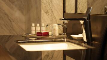 Un meuble-lavabo de salle de bain avec un plan de toilette en marbre, un évier et un miroir. On y trouve plusieurs articles de toilette, notamment des flacons et une boîte rouge.
