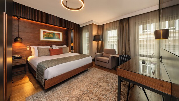 Una habitación de hotel moderna con una cama grande, un escritorio, una silla y un aparador de vidrio.