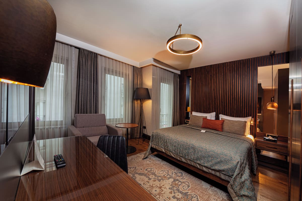 A modern hotel room with a large bed, a desk, and a sofa.