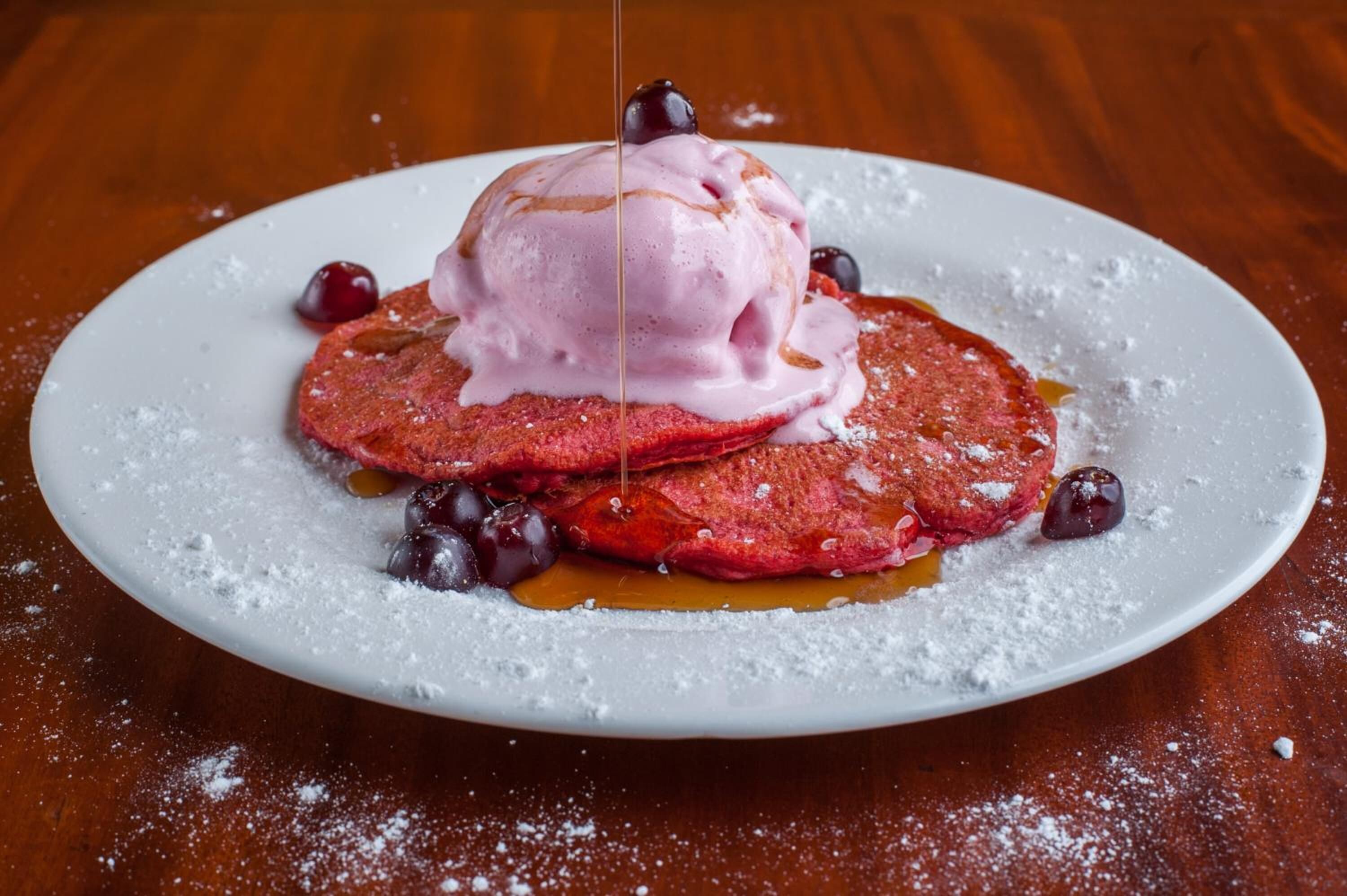 A plate of pancakes with a scoop of ice cream and syrup, garnished with cherries and blueberries.