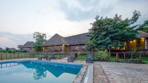 A resort with a swimming pool, thatched-roof cottages, and lush greenery.