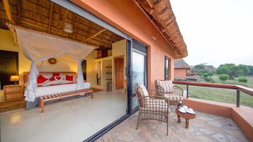 Relax in a serene bedroom with a large bed, wooden bench, and balcony overlooking a lush landscape.