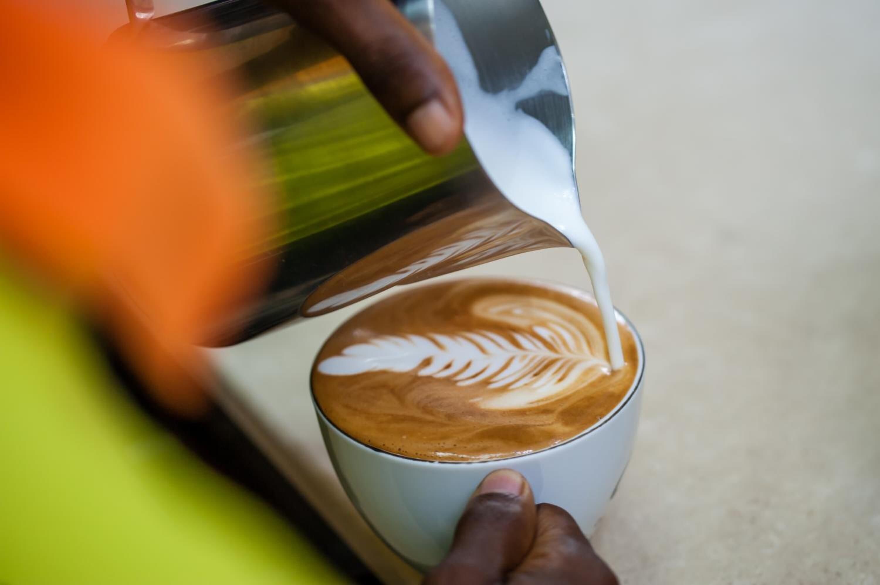 Una persona versa latte in una tazza di caffè con decorazione a latte art.