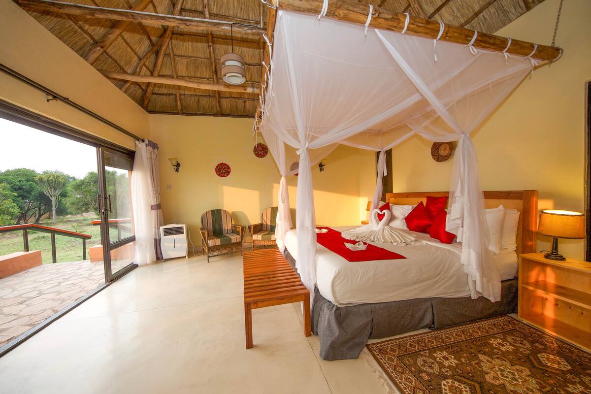 Una habitación con una cama, un banco, una silla, una mesita de noche y vistas al exterior.