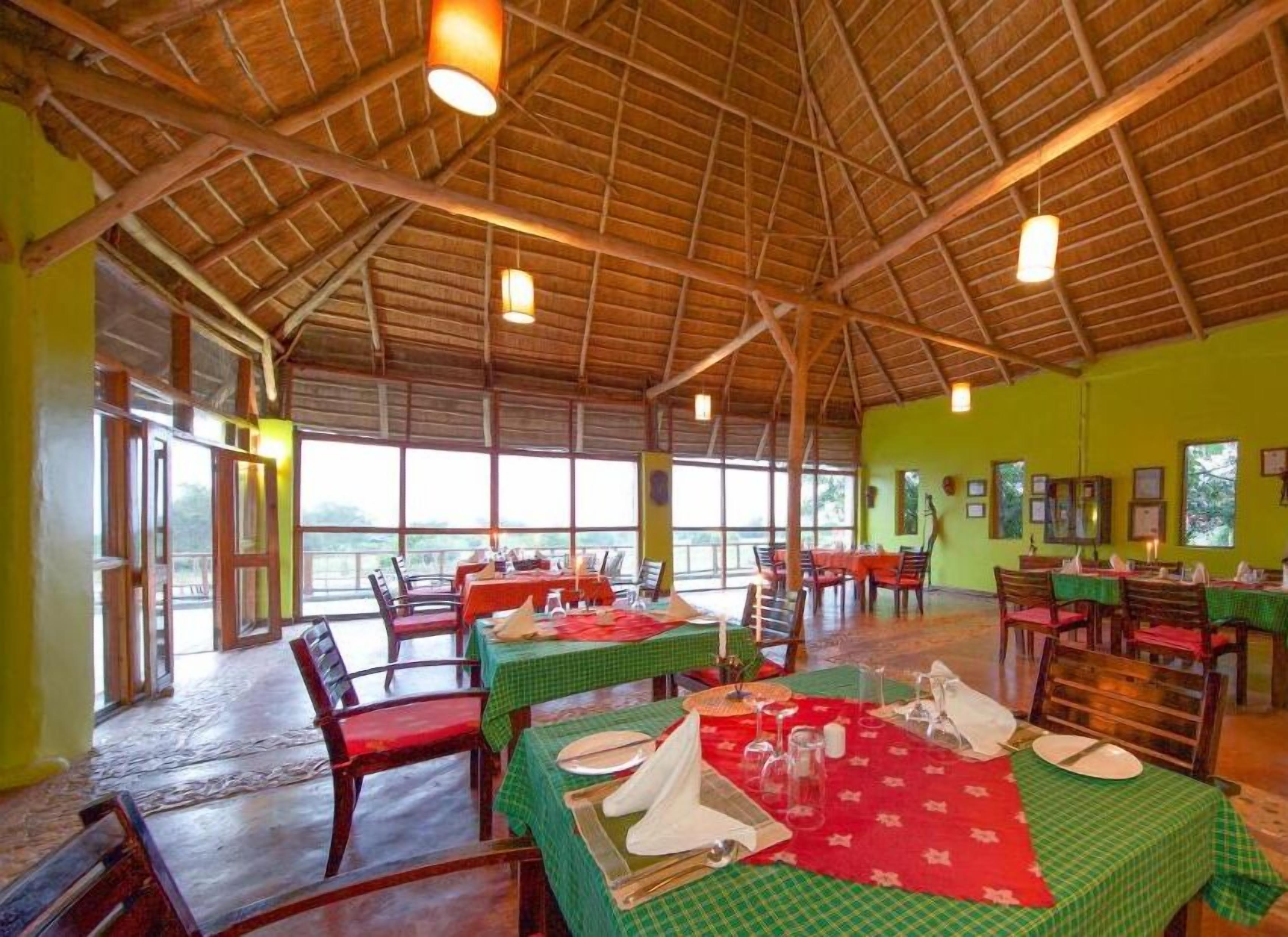 A spacious dining area with tables set for meals, large windows, and a high wooden ceiling.