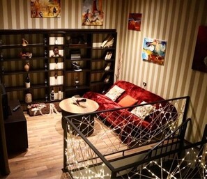 Una sala de estar acogedora con un sofá rojo, una mesa de centro y una estantería llena de libros y objetos decorativos.
