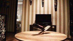A room with a round wooden table, a black TV on a stand, and a striped wall with three decorative masks. - Apartment on Aghmashenebeli Ave. (Tbilisi)