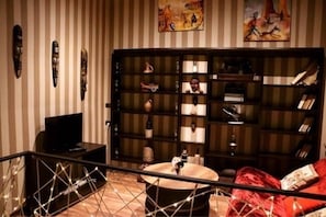 A room with a striped wall, a bookshelf with various items, a round table, and a red sofa. - Apartment on Aghmashenebeli Ave. (Tbilisi)
