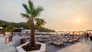 Zona de playa con filas de tumbonas y sombrillas, un macetero con palmeras y vistas al mar al atardecer.