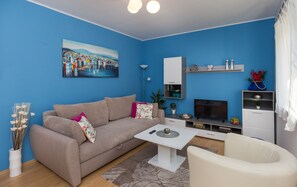 Ett vardagsrum med en blå vägg, en beige soffa, ett vitt soffbord, en tv och ett skåp.