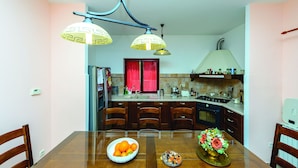 A modern kitchen with a dining table, chairs, and a bowl of fruit.