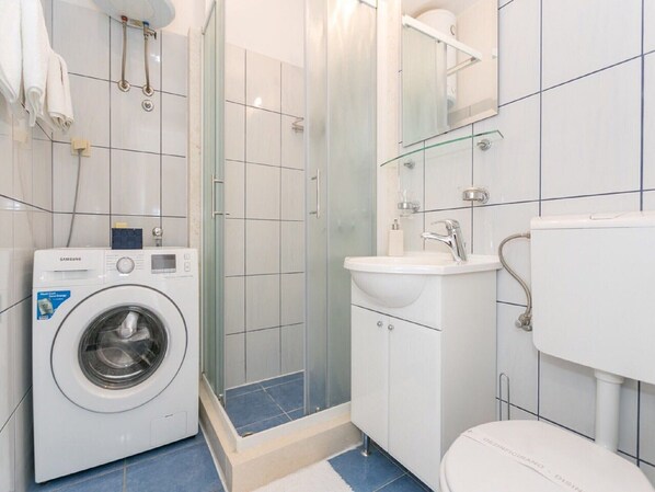 A modern bathroom with a washing machine, a glass shower enclosure, a sink, and a toilet.