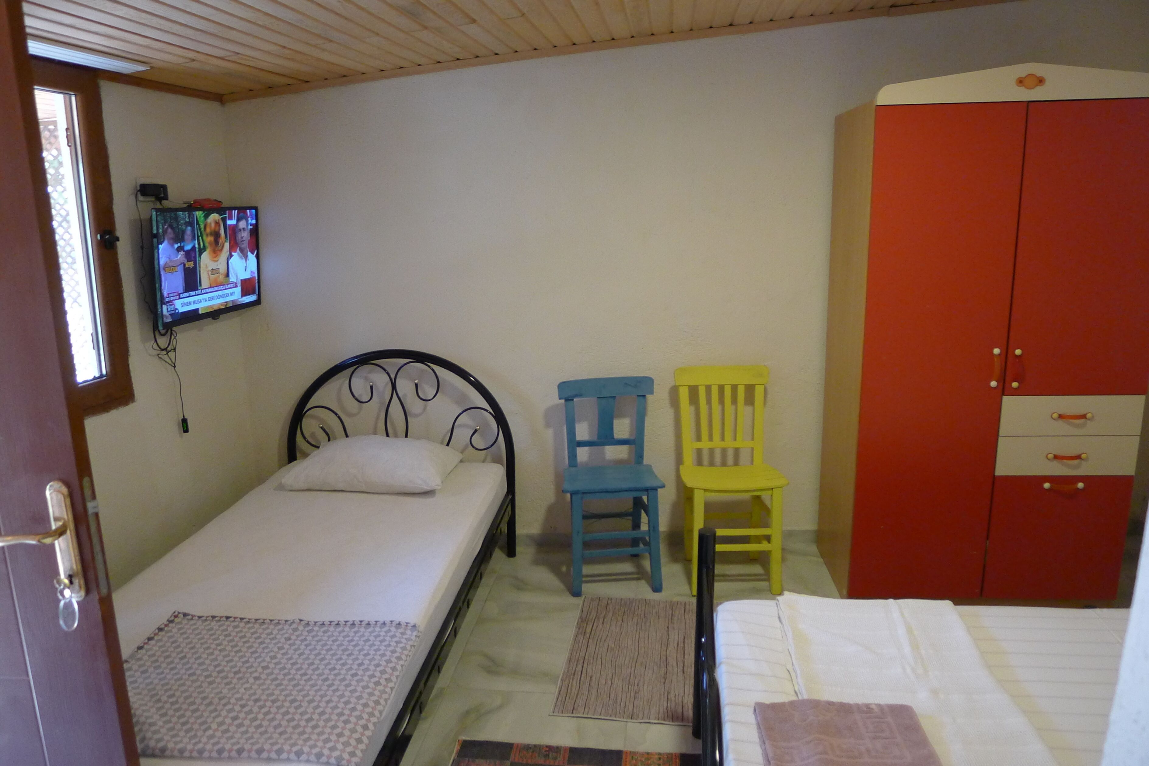 Un dormitorio con cama, televisor montado en la pared, armario y dos sillas.