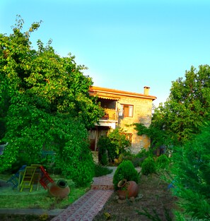 A stone house with a red-tiled roof, surrounded by lush greenery and a paved pathway. - Yesildag Pansiyon Gokceada (Gökçeada)