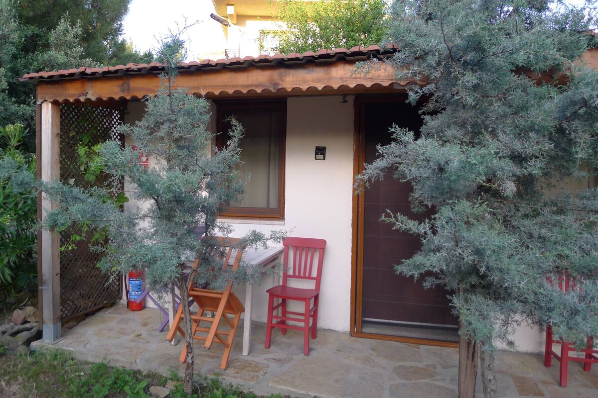A small building with a tiled roof, a wooden door, and a window. There is a chair and a table outside.