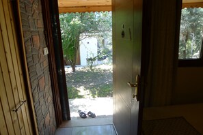 An open door leading to a courtyard with a tree, a white building, and a pair of shoes on the ground. - Yesildag Pansiyon Gokceada (Gökçeada)