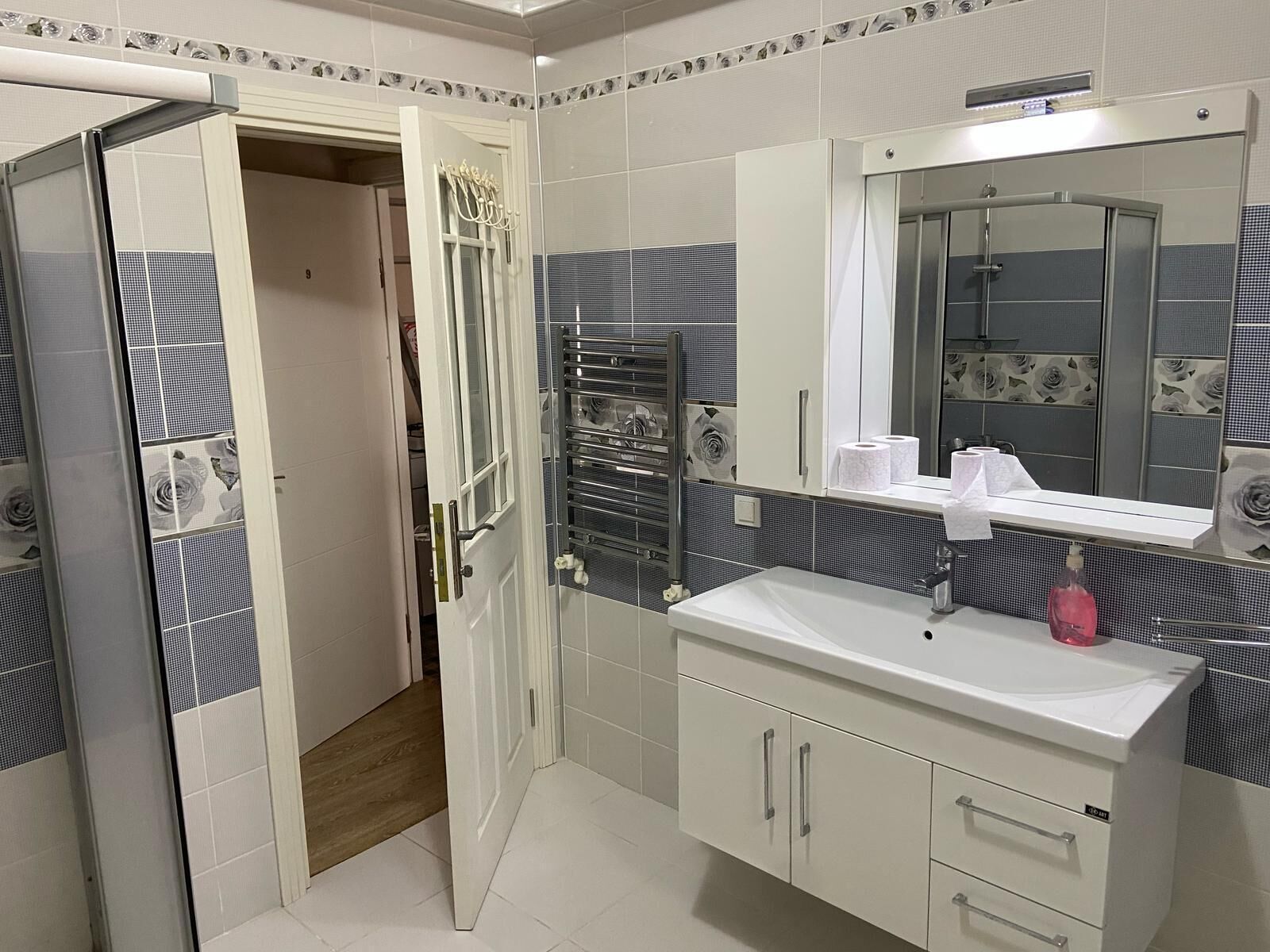 Une salle de bain moderne avec un lavabo blanc, un grand miroir et un espace douche.