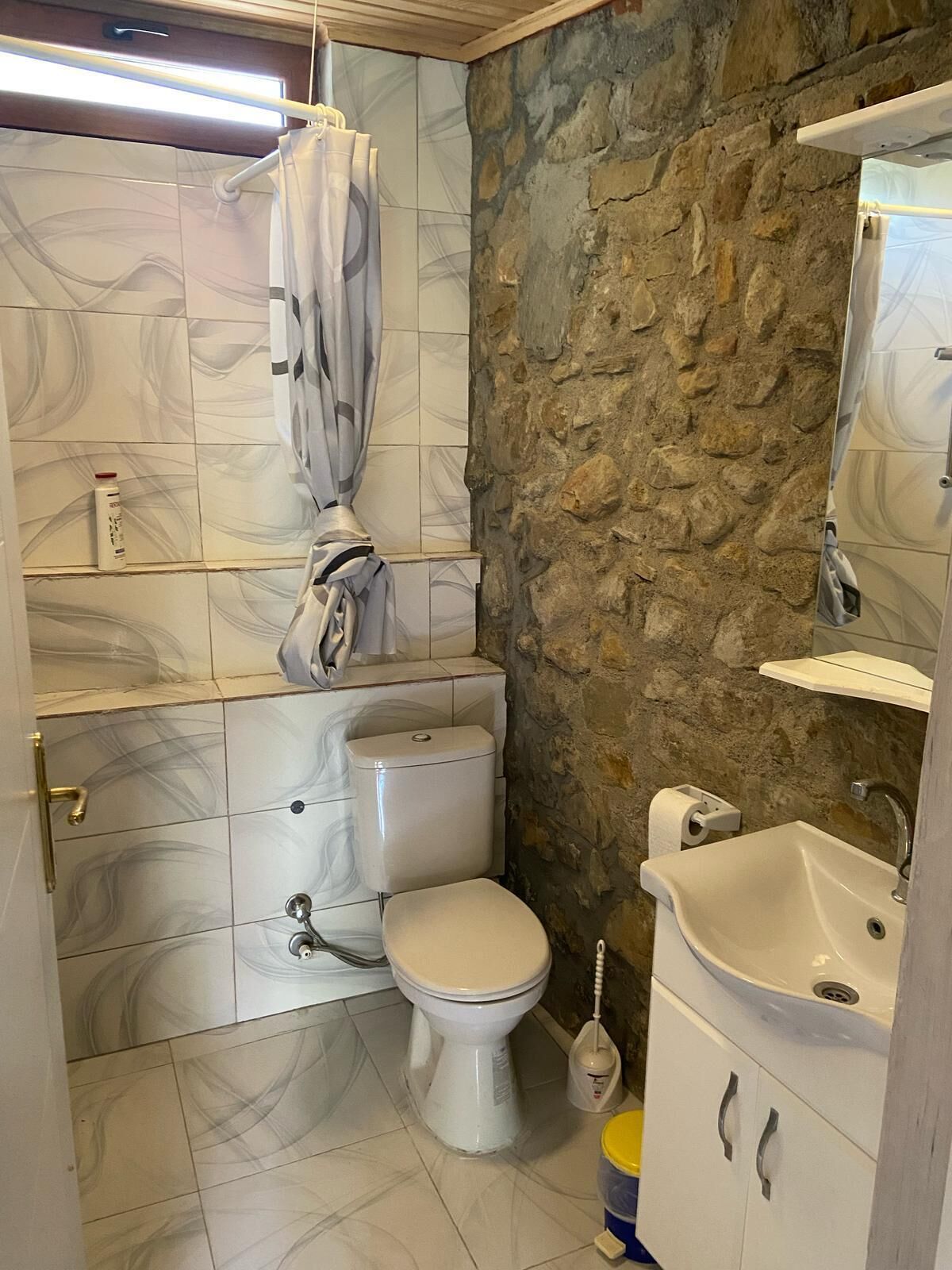 Un baño con inodoro, lavamanos y pared de piedra.