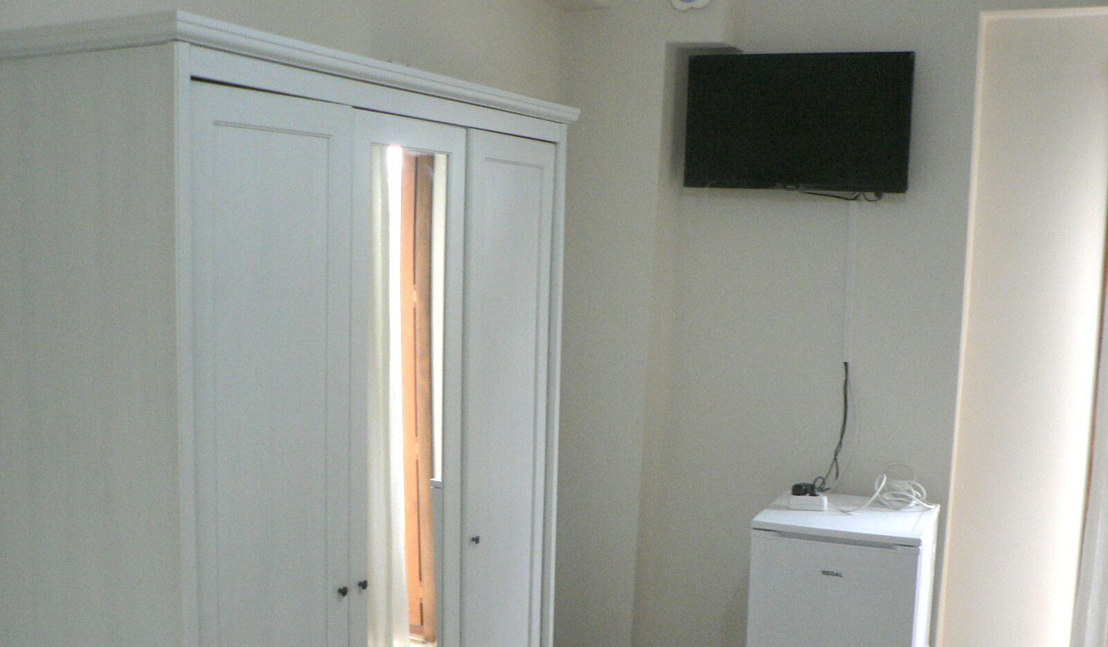 Una habitación con un armario blanco, un pequeño electrodoméstico blanco y un televisor montado.