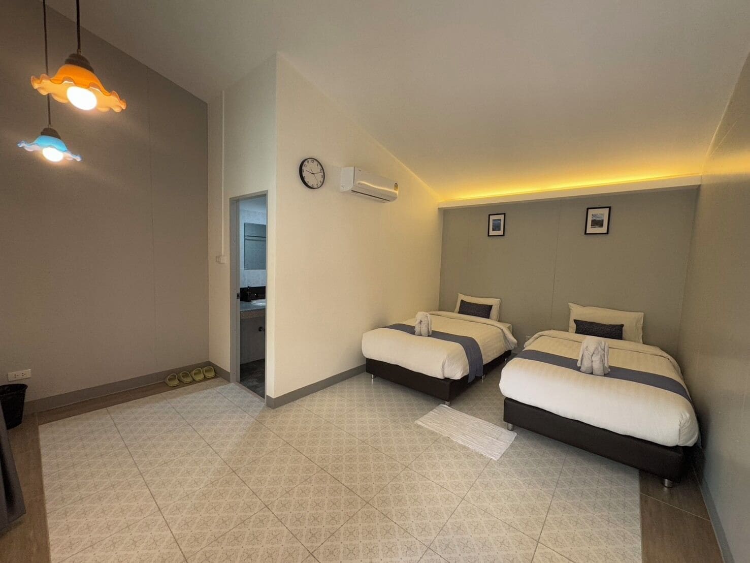 Habitación de hotel con dos camas, un reloj, aire acondicionado instalado en la pared y una puerta que da a un baño.