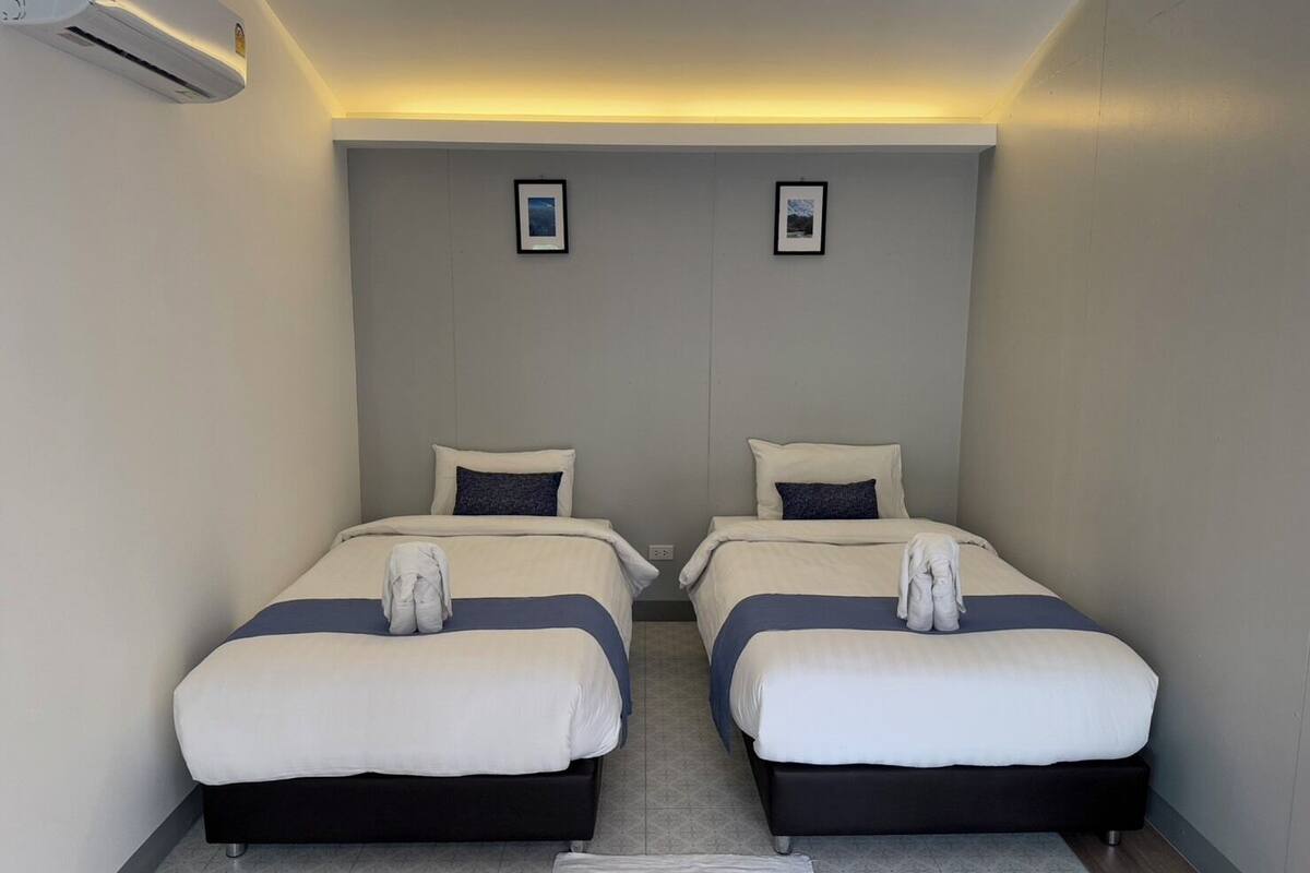 Quarto duplo com duas camas, cada uma com travesseiro e cobertor, e um tapete pequeno no chão.