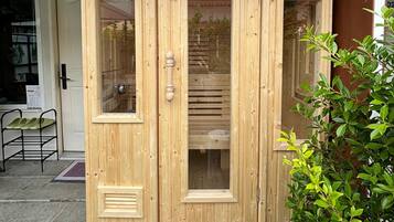A wooden sauna with glass doors, a small window, and a control panel on the right.