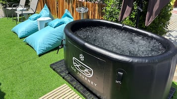 An outdoor ice bath with a wooden deck, blue cushions, and a wooden fence in the background.
