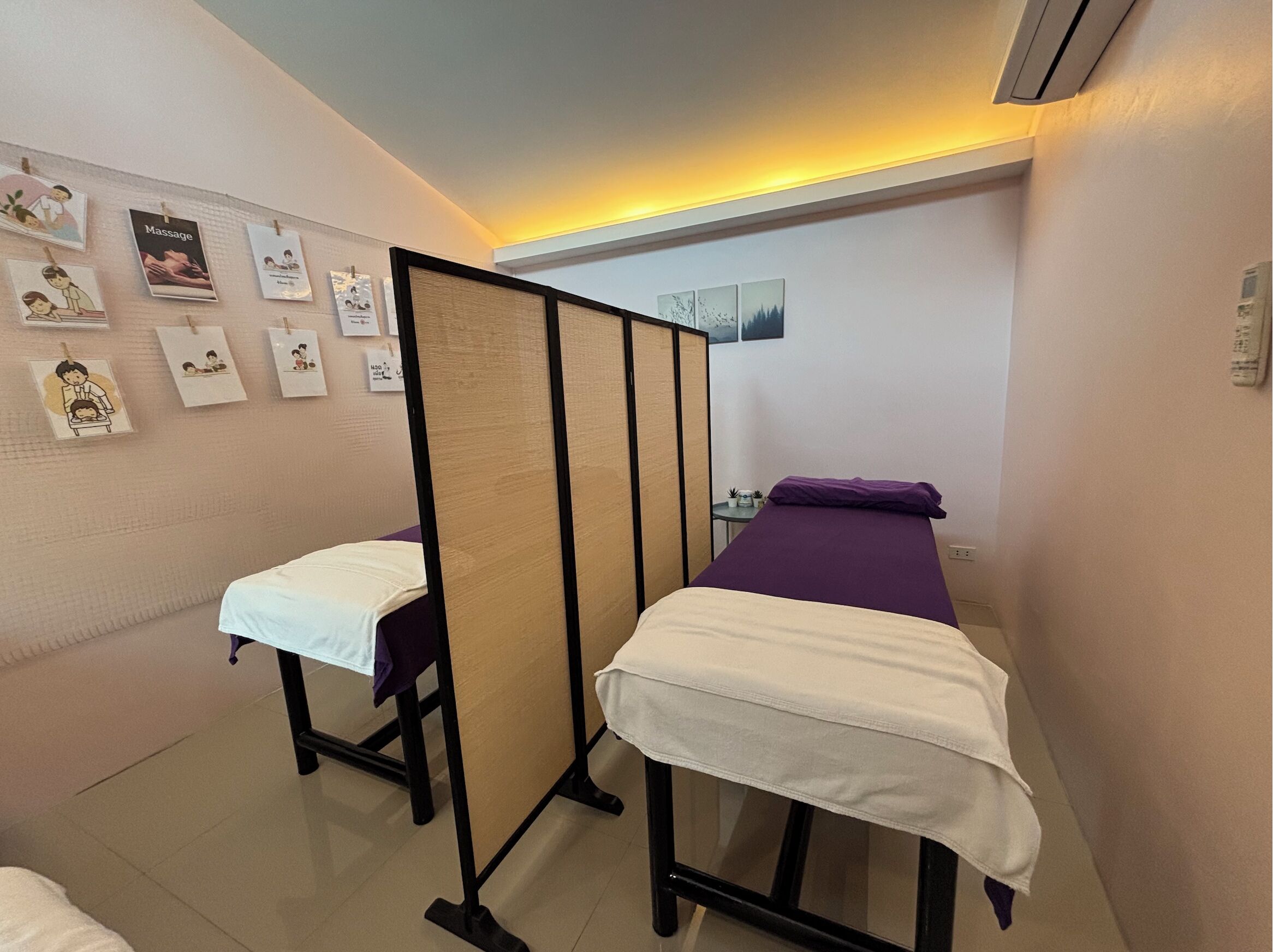 A room with two beds, a partition, and a wall with framed pictures.