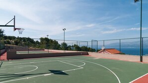 An outdoor basketball court with a clear view of the sea in the background.