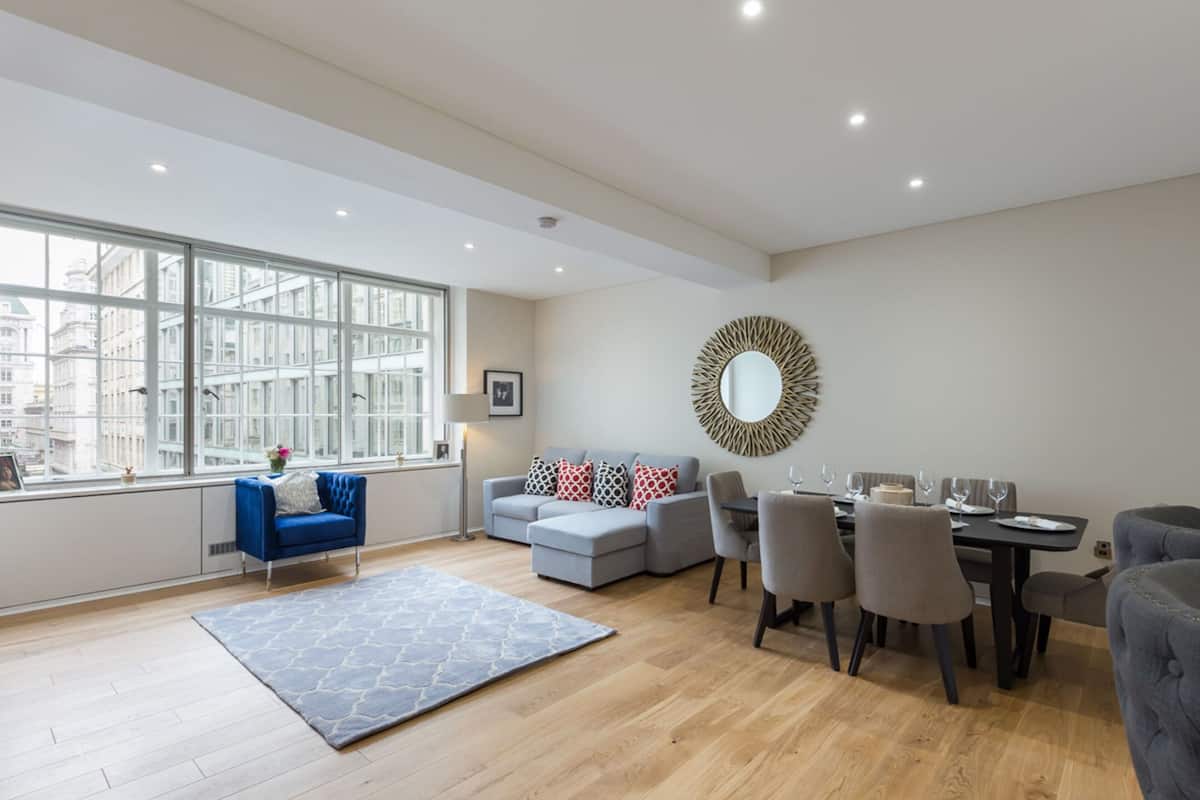 A modern living room with a large window, a dining area, and a grey sofa.